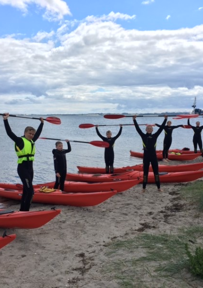 7 unge på en strand med røde kajakker liggende i vandkanten