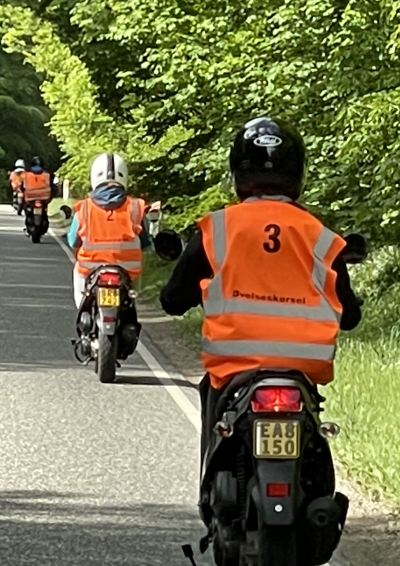 fire knallert kører gennem en skov med orange veste på 