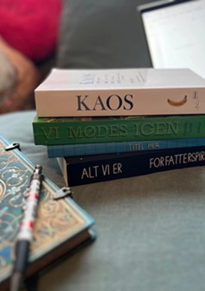 tre billeder ligger på et bord i en stak, foran ligger en enkelt med møster på og med en kuglepen ovenpå