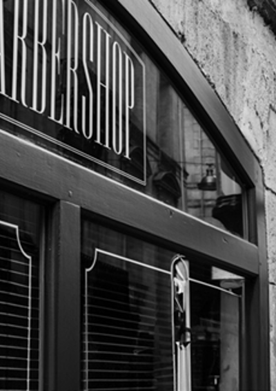 en barbarshop set ude fra. Røde mursten og et skilt hvor der står barbershop