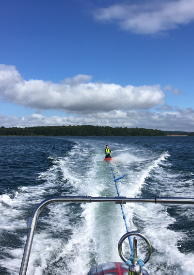 En person på kneeboard efter en speedbåd på havet, blå himmel.