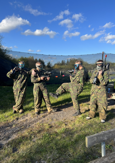 Fire unge i kamuflagedragter foran en paintball bane