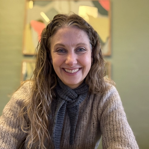 dame med lagt krøllet hår sidder foran en grøn væg