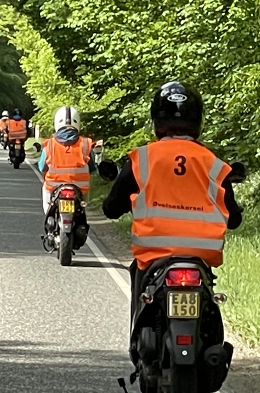 Fre knallerter, kører på en vej. førerne har orange veste på. 