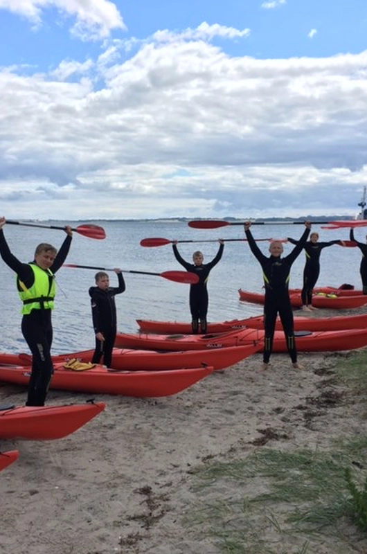 7 unge på en strand med røde kajakker liggende i vandkanten
