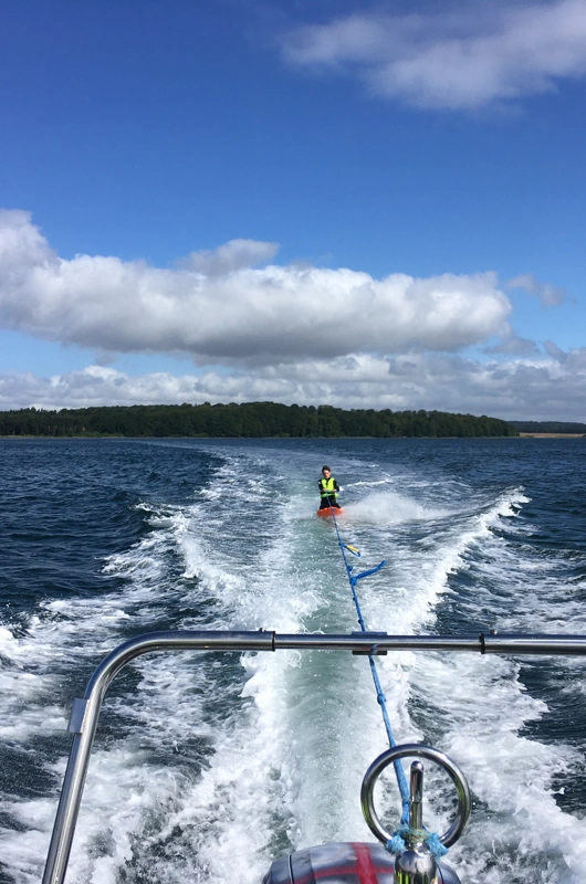 En person på kneeboard efter en speedbåd på havet, blå himmel.